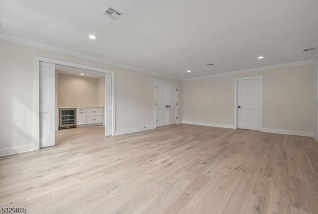 interior space featuring light wood-type flooring, visible vents, crown molding, and baseboards