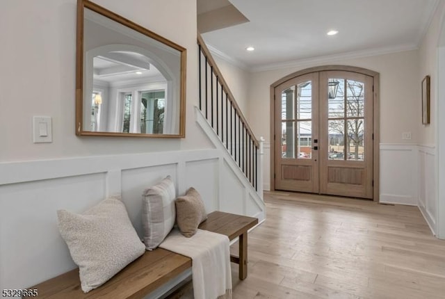 entrance foyer featuring light wood finished floors, arched walkways, wainscoting, ornamental molding, and french doors