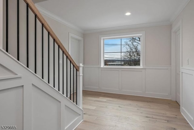 entryway featuring a wainscoted wall, crown molding, a decorative wall, light wood-style flooring, and stairway