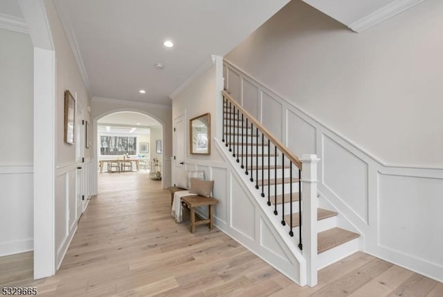 staircase featuring crown molding, arched walkways, a decorative wall, and wood finished floors