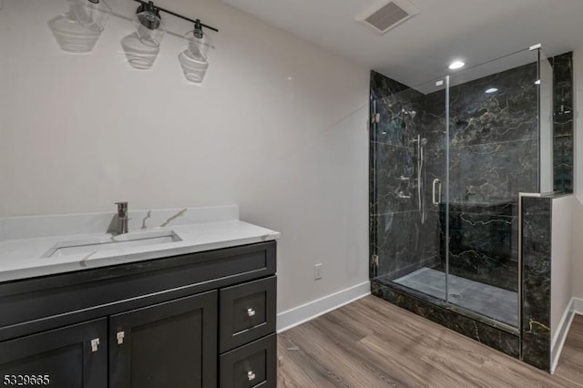 bathroom with wood finished floors, vanity, visible vents, baseboards, and a marble finish shower