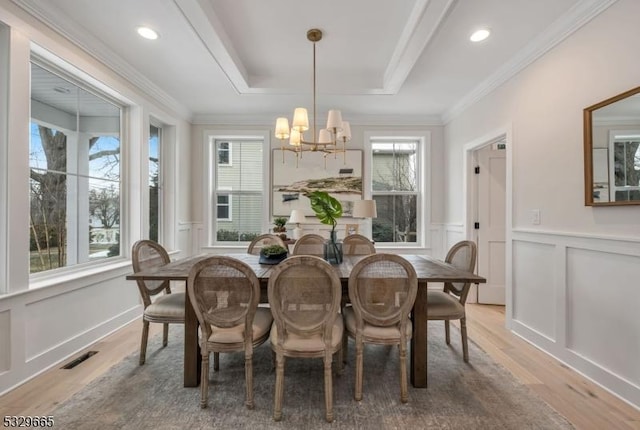 dining room featuring a decorative wall, visible vents, light wood-style floors, ornamental molding, and a raised ceiling