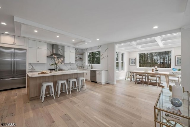 kitchen with white cabinets, wall chimney exhaust hood, a kitchen island, appliances with stainless steel finishes, and light countertops