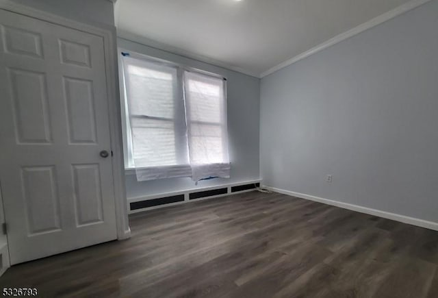 empty room featuring ornamental molding, a baseboard heating unit, and dark wood-type flooring