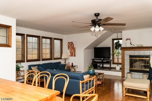 living area with ceiling fan, a tiled fireplace, and wood finished floors