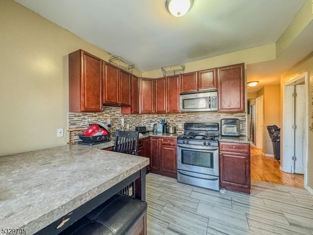 kitchen with backsplash, kitchen peninsula, a breakfast bar area, and appliances with stainless steel finishes