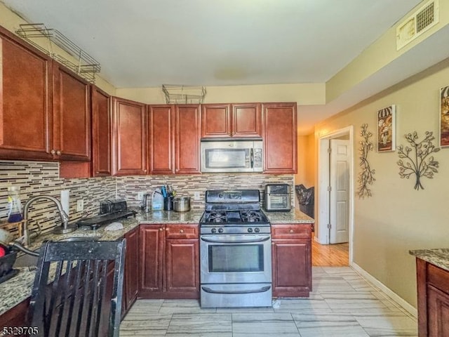 kitchen featuring tasteful backsplash, stone counters, sink, and appliances with stainless steel finishes