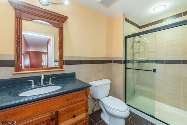 bathroom featuring toilet, a shower with shower door, tile walls, vanity, and tile patterned flooring