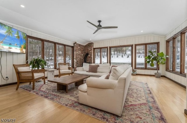 sunroom / solarium featuring ceiling fan, plenty of natural light, a wood stove, and lofted ceiling