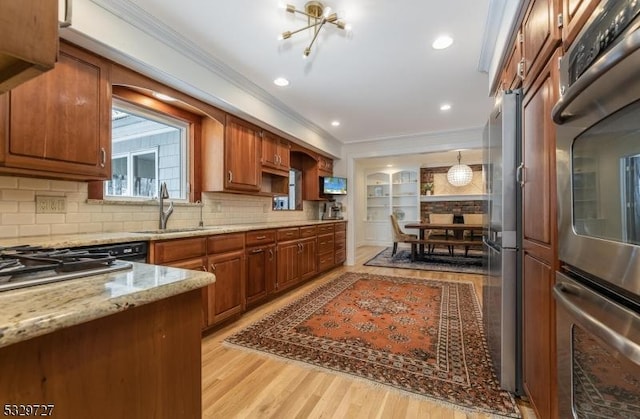 kitchen featuring crown molding, light stone countertops, hanging light fixtures, light wood-type flooring, and sink