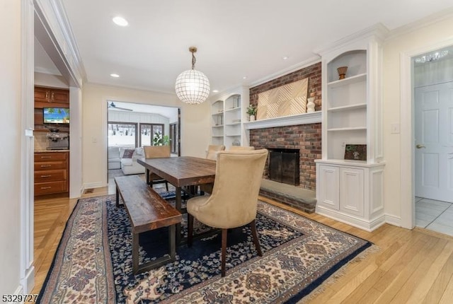 dining area featuring built in shelves, a chandelier, light wood-type flooring, a brick fireplace, and crown molding