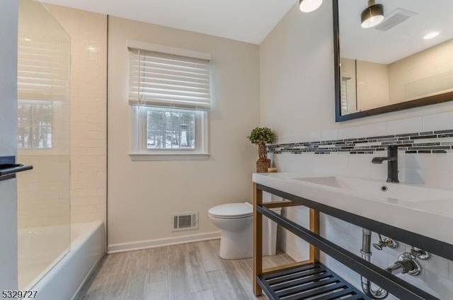 full bathroom featuring tiled shower / bath combo, sink, hardwood / wood-style flooring, tasteful backsplash, and toilet