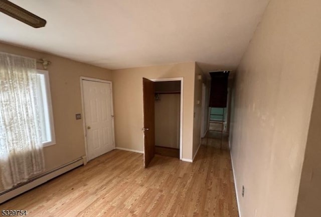 unfurnished bedroom with light wood-type flooring, a baseboard radiator, multiple windows, and ceiling fan