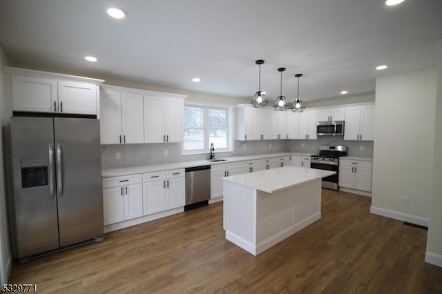 kitchen featuring appliances with stainless steel finishes, sink, white cabinets, a center island, and hanging light fixtures