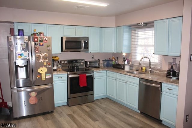 kitchen featuring light stone countertops, sink, light hardwood / wood-style flooring, and appliances with stainless steel finishes