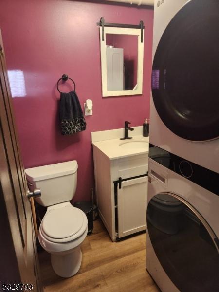 bathroom with hardwood / wood-style flooring, vanity, toilet, and stacked washer / dryer