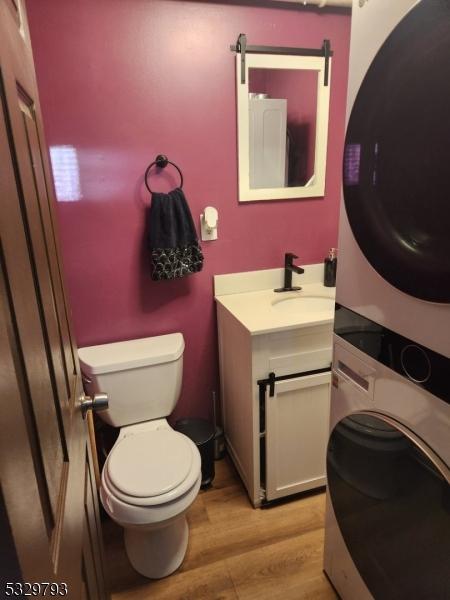 bathroom featuring stacked washer / drying machine, toilet, wood-type flooring, and vanity