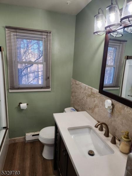 bathroom with an inviting chandelier, baseboard heating, toilet, vanity, and hardwood / wood-style flooring