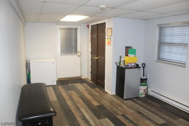 interior space featuring dark hardwood / wood-style flooring, a baseboard radiator, and a drop ceiling