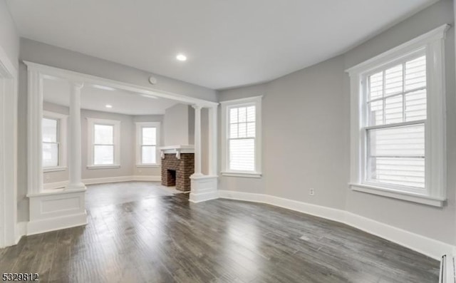 unfurnished living room with dark hardwood / wood-style flooring, ornate columns, and a brick fireplace