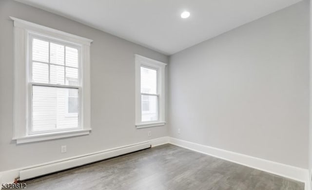 unfurnished room featuring baseboard heating, a wealth of natural light, and hardwood / wood-style flooring