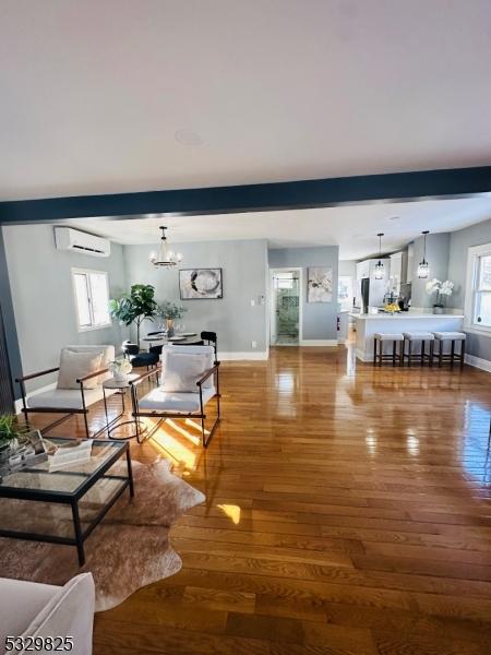 living room featuring hardwood / wood-style flooring, plenty of natural light, a wall unit AC, and a chandelier