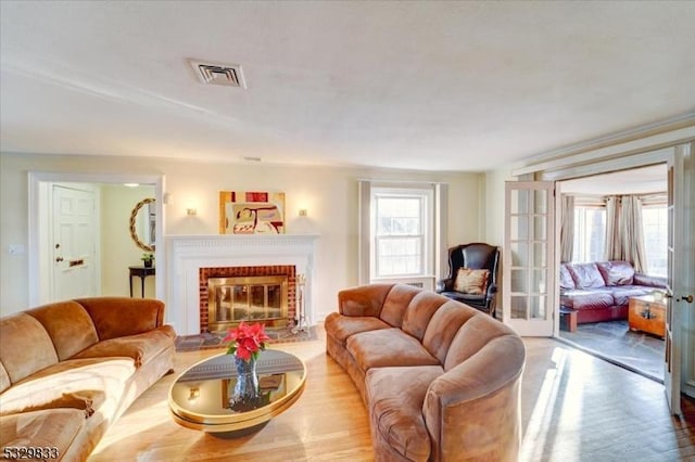 living room with french doors, light wood-type flooring, and a brick fireplace