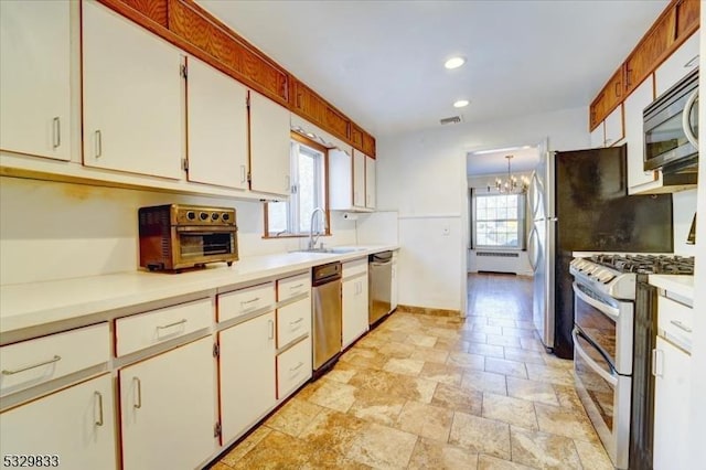 kitchen featuring radiator, white cabinetry, sink, a notable chandelier, and appliances with stainless steel finishes