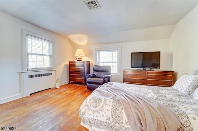 bedroom featuring radiator heating unit, light hardwood / wood-style flooring, and multiple windows