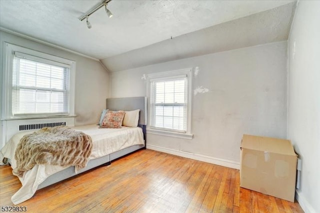 bedroom with light hardwood / wood-style flooring, track lighting, and vaulted ceiling