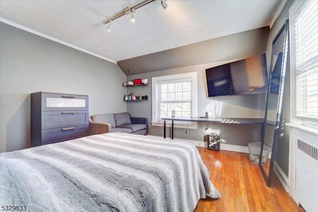 bedroom with rail lighting, ornamental molding, vaulted ceiling, radiator heating unit, and light hardwood / wood-style floors