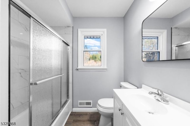 full bathroom featuring shower / bath combination with glass door, vanity, wood-type flooring, and toilet