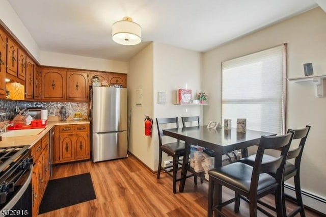 kitchen with hardwood / wood-style flooring, a baseboard heating unit, decorative backsplash, sink, and stainless steel appliances