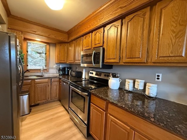 kitchen with stainless steel appliances, light hardwood / wood-style flooring, dark stone counters, and sink