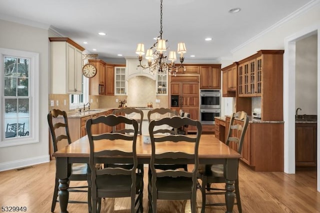 dining space with crown molding, sink, a notable chandelier, and light wood-type flooring