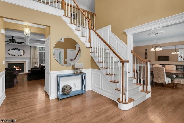 stairs with hardwood / wood-style flooring, coffered ceiling, ceiling fan with notable chandelier, and beamed ceiling