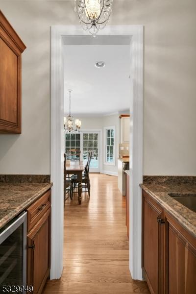 kitchen featuring an inviting chandelier, beverage cooler, light wood-type flooring, and dark stone countertops