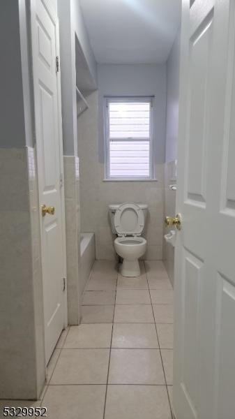 bathroom with toilet, a bath, tile patterned floors, and tile walls