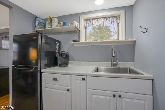 kitchen with white cabinets, black refrigerator, and sink