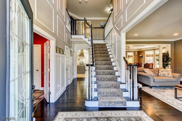 foyer with crown molding, decorative columns, dark hardwood / wood-style floors, and a towering ceiling