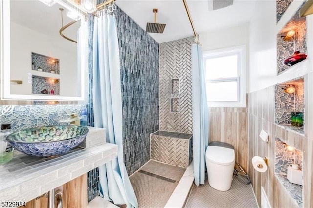 bathroom featuring tile patterned floors, a tile shower, tile walls, and toilet