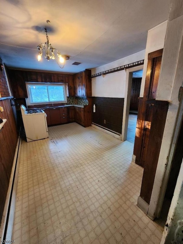 kitchen with an inviting chandelier, baseboard heating, a barn door, wood walls, and dark brown cabinets