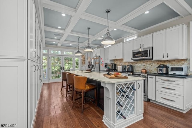 kitchen featuring appliances with stainless steel finishes, a kitchen breakfast bar, a center island with sink, white cabinets, and hanging light fixtures