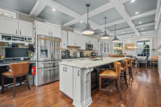 kitchen with pendant lighting, a kitchen island with sink, white cabinets, a kitchen bar, and stainless steel appliances