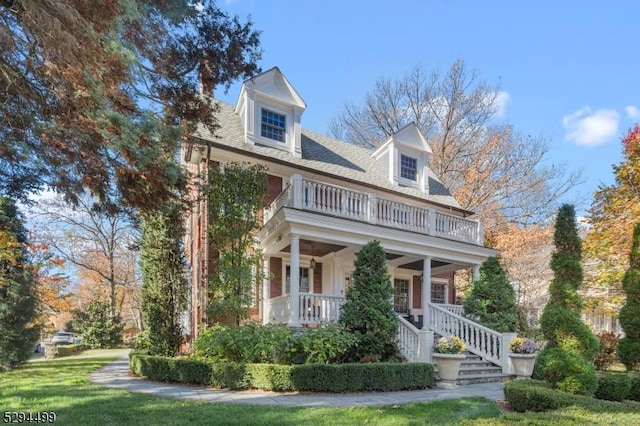 cape cod-style house with covered porch, a balcony, and a front lawn