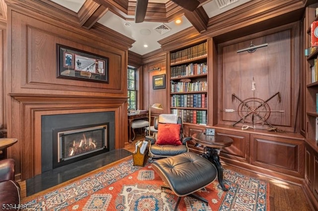 sitting room with beam ceiling, coffered ceiling, built in features, crown molding, and wood walls