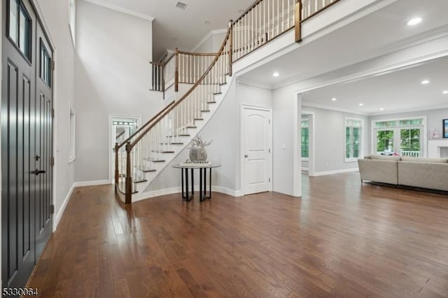 foyer featuring a towering ceiling, stairway, hardwood / wood-style floors, ornamental molding, and baseboards