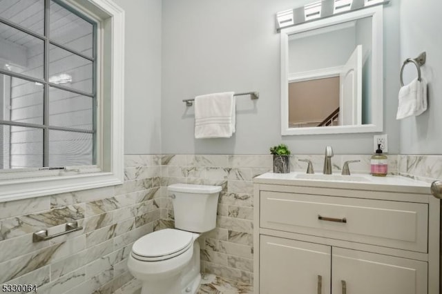 half bath with toilet, wainscoting, vanity, and tile walls