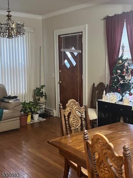 dining space featuring a baseboard heating unit, an inviting chandelier, ornamental molding, and hardwood / wood-style floors