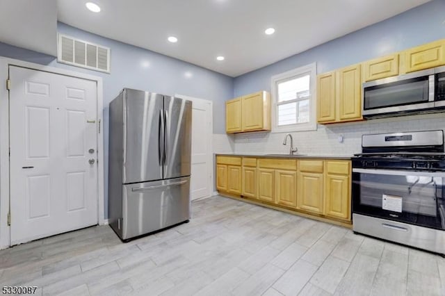 kitchen with sink, backsplash, light brown cabinetry, appliances with stainless steel finishes, and light wood-type flooring